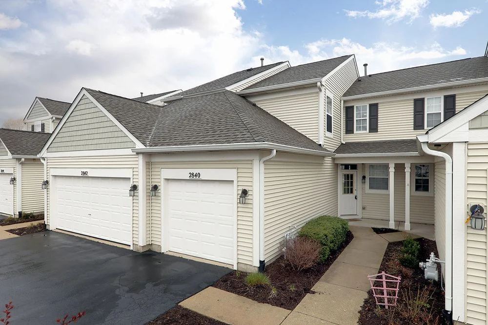 Exterior of attached townhomes in the Windridge neighborhood of Naperville, featuring beige siding, private garages, and landscaped walkways.